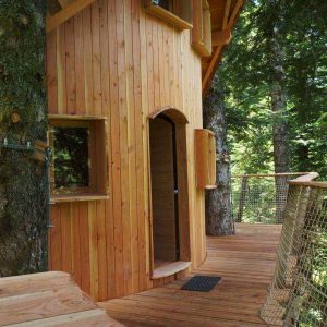 Cabane perchée en bois dans les arbres, entourée de verdure et de nature.