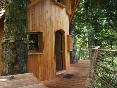 Cabane perchée en bois dans les arbres, entourée de verdure et de nature.
