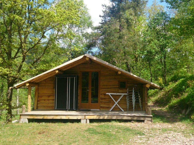 Cabane en bois dans la nature, avec terrasse et vue sur la forêt verdoyante.