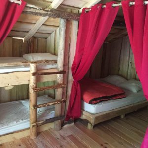 Hébergement insolite en cabane avec lits superposés et rideaux rouges chaleureux.