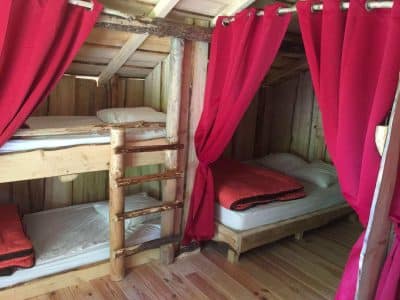Hébergement insolite en cabane avec lits superposés et rideaux rouges chaleureux.