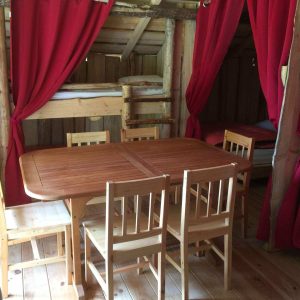 Cabane en bois avec table en bois et rideaux rouges, idéale pour un séjour unique.