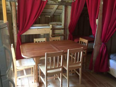 Cabane en bois avec table en bois et rideaux rouges, idéale pour un séjour unique.