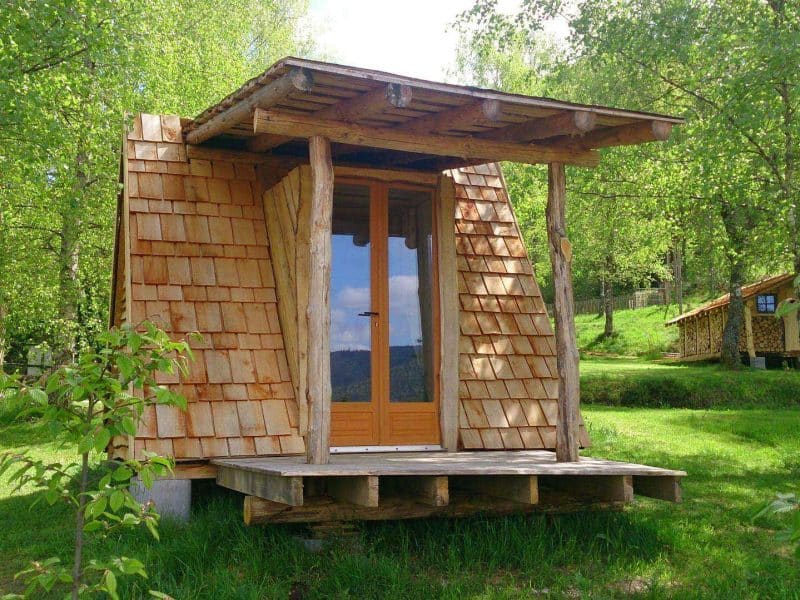 Cabane en bois au toit en ardoise, nichée dans la verdure du Grand-Est.