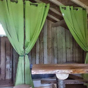Cabane en bois avec rideaux verts, offrant un séjour insolite en Grand-Est.