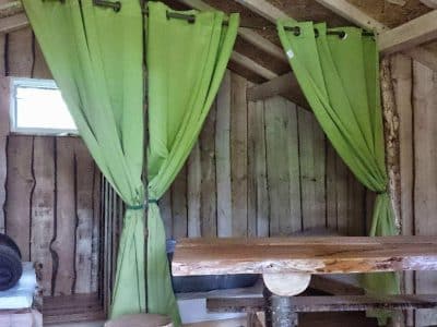 Cabane en bois avec rideaux verts, offrant un séjour insolite en Grand-Est.