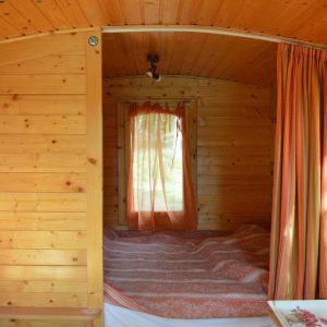 Intérieur chaleureux dune roulotte en bois, avec rideaux orange et lit douillet.