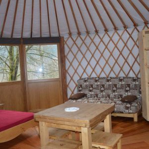 Yourte spacieuse en bois avec un lit confortable et de grandes fenêtres lumineuses.