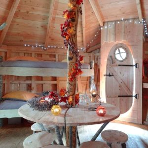 Cabane en bois avec décor automnal, table ronde et lits superposés confortables.