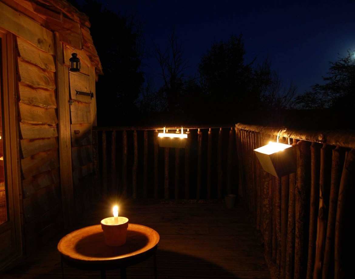 Cabane perchée au Centre, éclairée par des bougies sous la lune. Ambiance cosy.