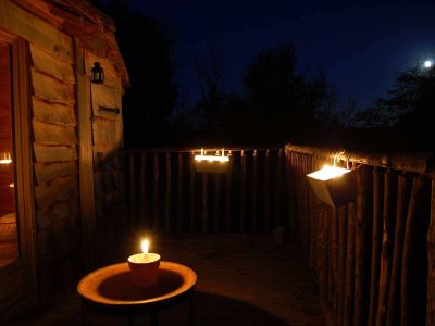 Cabane perchée au Centre, éclairée par des bougies sous la lune. Ambiance cosy.
