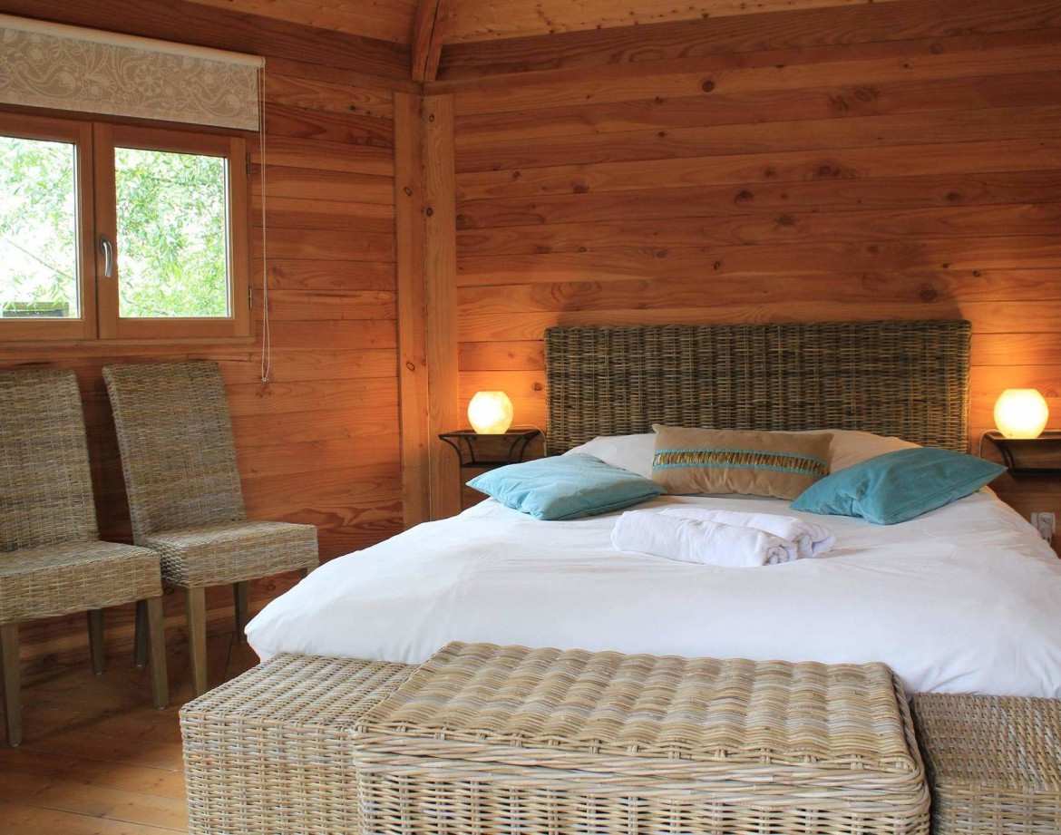 Chalet en bois chaleureux avec lit douillet et chaises en osier. Parfait pour un séjour relaxant.