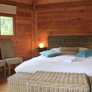 Chalet en bois chaleureux avec lit douillet et chaises en osier. Parfait pour un séjour relaxant.