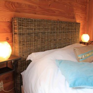 Chambre en bois avec tête de lit en osier et lampes lumineuses douces.