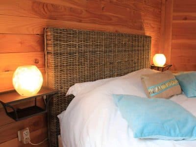 Chambre en bois avec tête de lit en osier et lampes lumineuses douces.