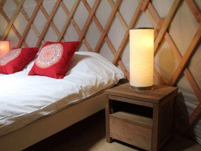 Chambre dans une yourte, lit douillet avec coussins rouges et lampes modernes.