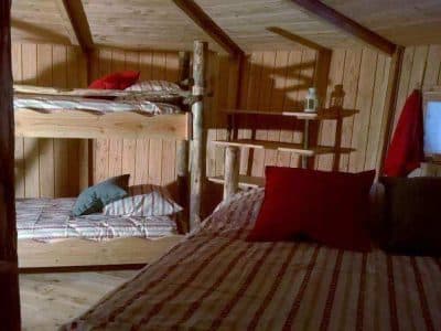 Cabane en bois avec lits superposés et coussins colorés, ambiance chaleureuse.