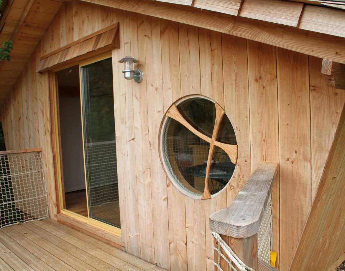 Cabane en bois avec une grande fenêtre ronde, située en Auvergne-Rhône-Alpes.