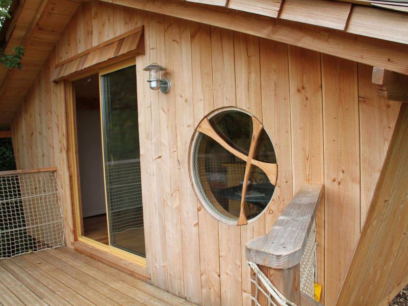 Cabane en bois avec une grande fenêtre ronde, située en Auvergne-Rhône-Alpes.