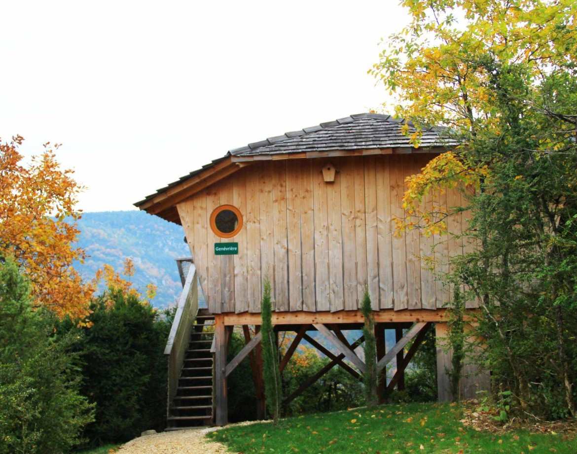 Cabane perchée en bois, entourée de verdure et darbres aux couleurs dautomne.