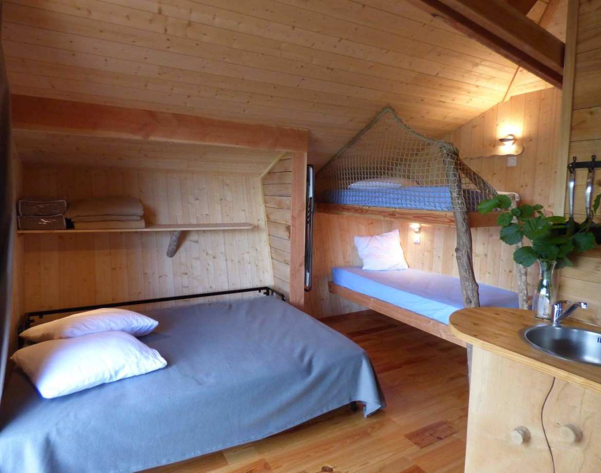 Cabane en bois avec lit double et mezzanine, ambiance chaleureuse et naturelle.