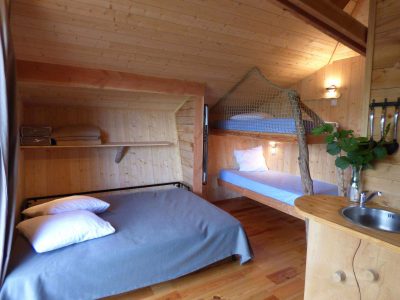 Cabane en bois avec lit double et mezzanine, ambiance chaleureuse et naturelle.