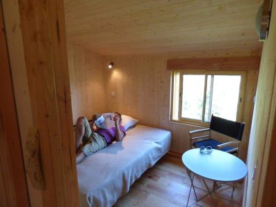 Chalet en bois chaleureux avec lit simple et coin lecture lumineux.