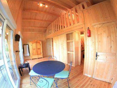 Cabane en bois chaleureuse avec mezzanine et coin repas convivial.