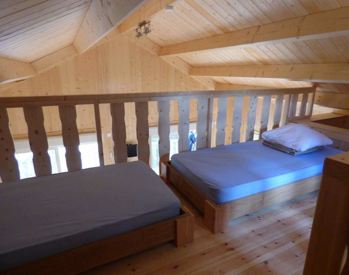 Chalet en bois avec lits simples, ambiance chaleureuse et lumineuse en Auvergne-Rhône-Alpes.