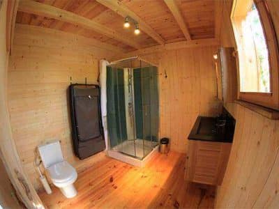 Cabane en bois avec salle de bain moderne et éclairage chaleureux.