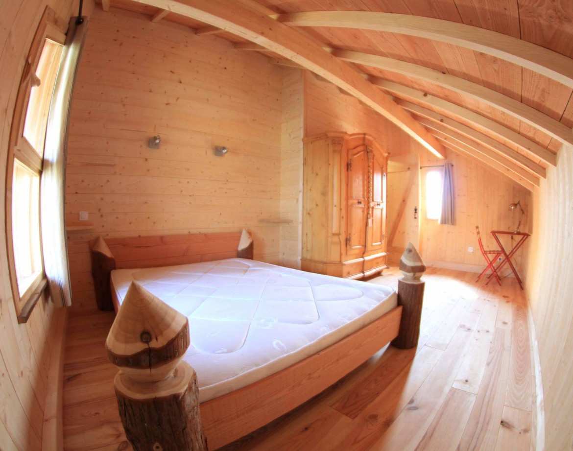 Chalet en bois chaleureux avec un lit douillet et des poutres apparentes.