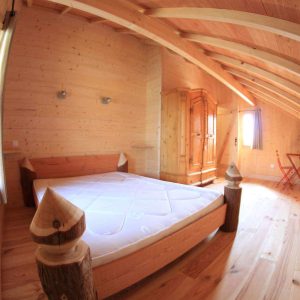 Chalet en bois chaleureux avec un lit douillet et des poutres apparentes.