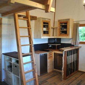 Cabane en bois avec mezzanine, cuisine équipée et échelle en bois. Ambiance chaleureuse.