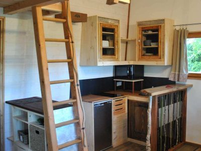 Cabane en bois avec mezzanine, cuisine équipée et échelle en bois. Ambiance chaleureuse.