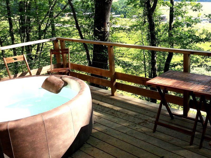 Cabane en bois avec jacuzzi sur une terrasse entourée darbres verdoyants.