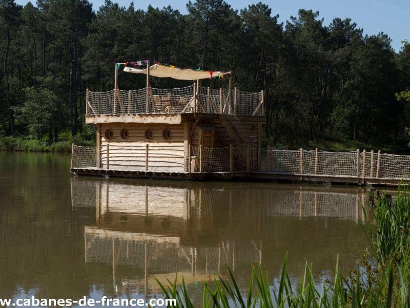 Cabane flottante en bois sur un lac, entourée de verdure et de calme.