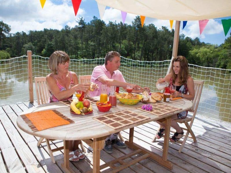 Table en bois au bord dun lac, trois personnes dégustent un repas convivial.