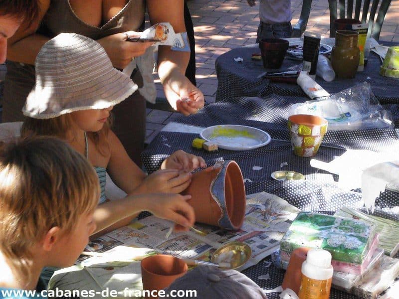 Atelier créatif en cabane, enfants décorant des pots en terre cuite.