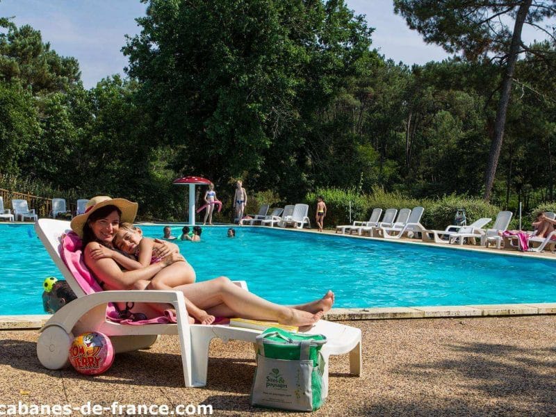Cabane de vacances avec piscine, transats et verdure environnante. Détente au soleil.