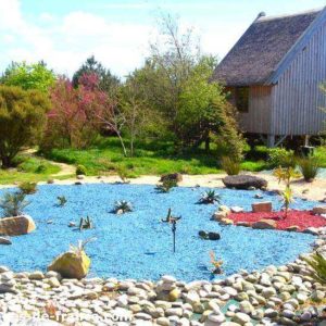 Chalet en bois entouré dun jardin coloré avec des pierres et des plantes exotiques.