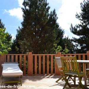 Cabane en bois avec terrasse ensoleillée entourée darbres verdoyants.