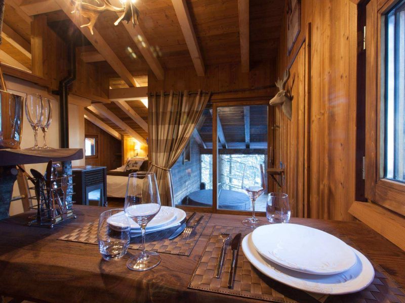 Chalet en bois chaleureux avec une table élégamment dressée et vue sur la montagne.
