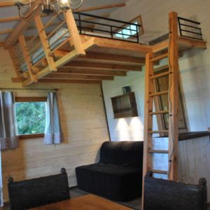 Chalet en bois avec mezzanine, intérieur chaleureux et mobilier en bois.