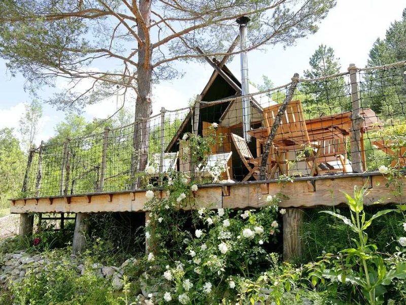 Cabane perchée en bois entourée de fleurs, avec terrasse ensoleillée en Auvergne-Rhône-Alpes.