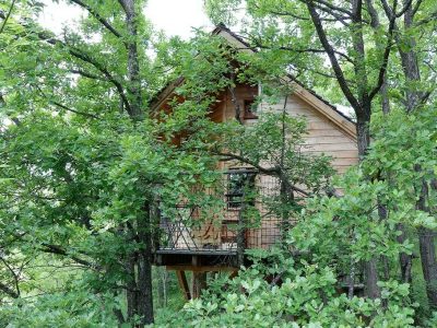 Cabane perchée dans les arbres, entourée de verdure luxuriante en Auvergne-Rhône-Alpes.