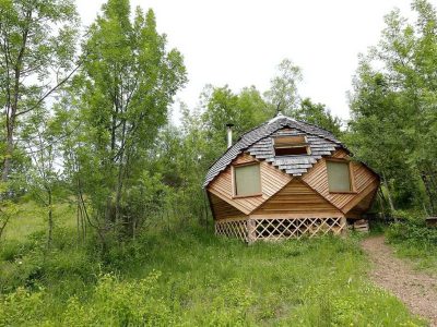Cabane en bois originale, entourée de verdure, avec un toit en ardoise.