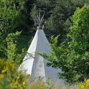 Tente tipi blanche entourée de verdure, idéale pour un séjour insolite en Auvergne-Rhône-Alpes.