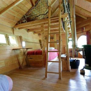 Cabane en bois avec échelle, lit confortable et poêle à bois chaleureux.