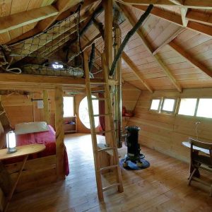 Cabane en bois avec mezzanine, lumière naturelle et décoration chaleureuse.