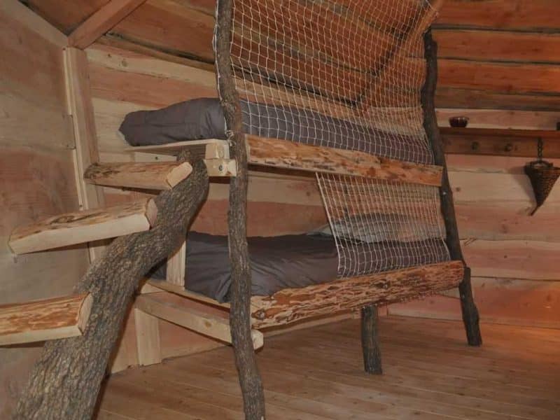 Cabane en bois avec lits superposés en rondins et échelle en bois naturel.